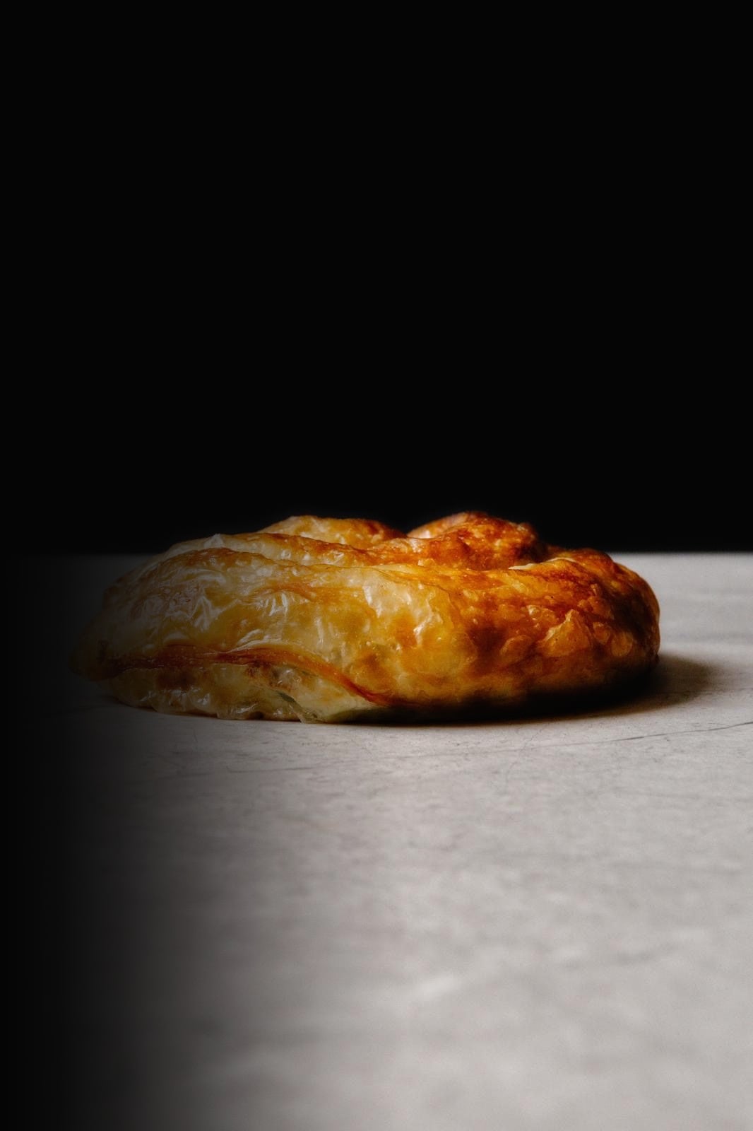 A golden, hand rolled burek on a stone bench against a black backdrop
